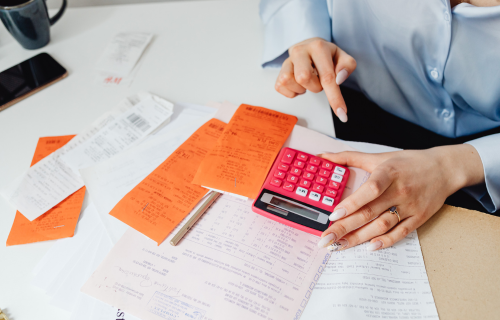 Woman using a calculator on a desk with papers and receipts
